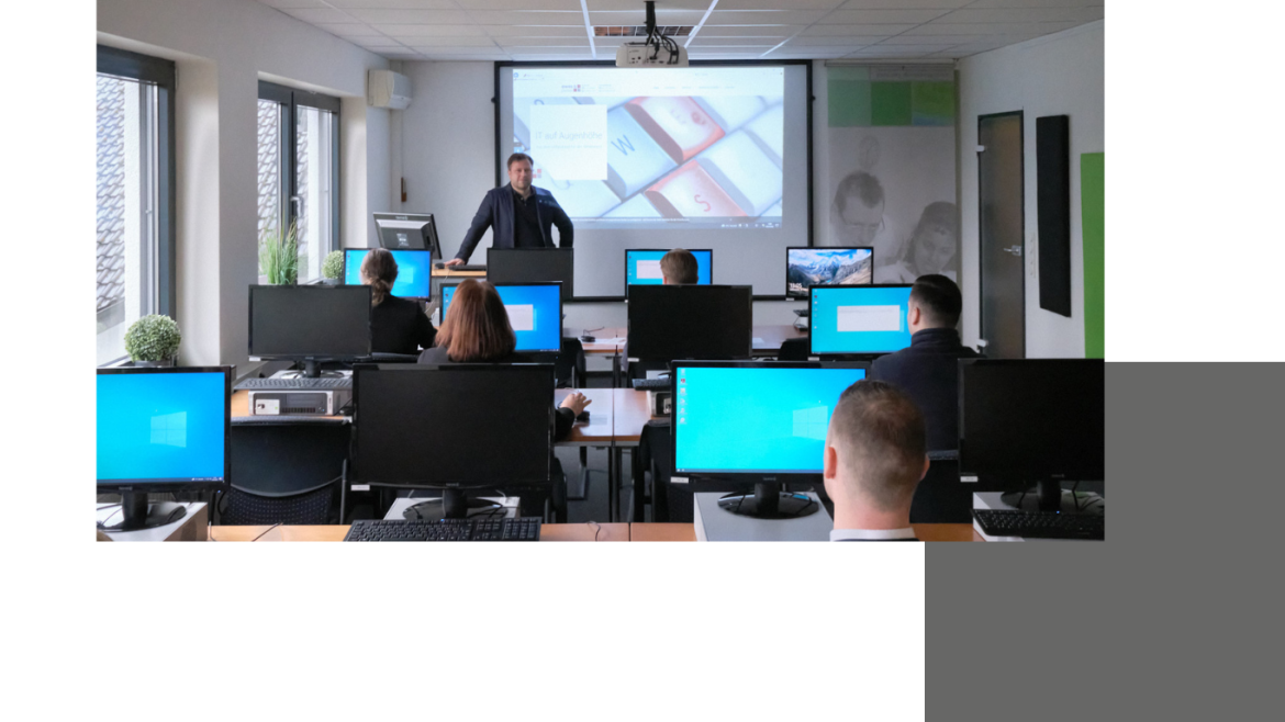 Blick in den Seminarraum, in dem einige Menschen an Computern sitzen und ein Referent vorne steht